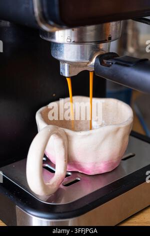 Espresso fresco versato dall'erogatore di una macchina da caffè in una tazza di ceramica, catturando il processo di preparazione di un caffè appena preparato. Foto Stock