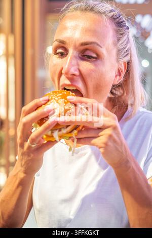 Donna che morde un hamburger, primo piano del cibo da asporto. Foto di alta qualità Foto Stock