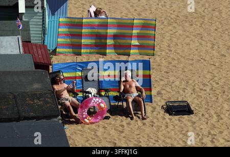 Vacanze estive e stile di vita da pensionati, coppia di anziani che si rilassa su sedie da spiaggia con frangivento colorato e anello gonfiabile su una spiaggia di sabbia durante il sole Foto Stock