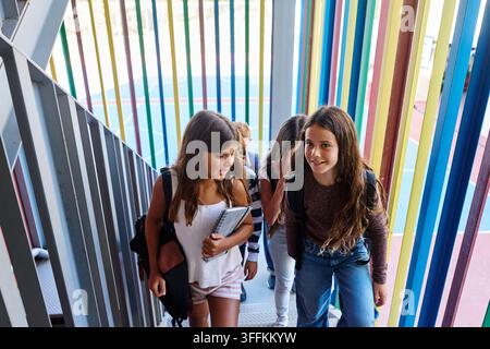 Gruppo di bambini con zaini e quaderni che salgono scale colorate in un edificio scolastico moderno Foto Stock