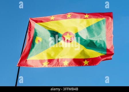 Bandiera di Grenada. Bandiera che sventola nel vento contro un cielo blu limpido, ondeggia su un’asta all’aperto. Giorno soleggiato, trama del tessuto, primo piano all’aperto- Foto Stock