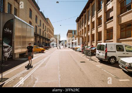 Kemptthal, Zurigo, Svizzera, 6 settembre 2026. Pedoni camminano lungo una strada all'aperto fiancheggiata da auto classiche e edifici industriali storici in mattoni Foto Stock