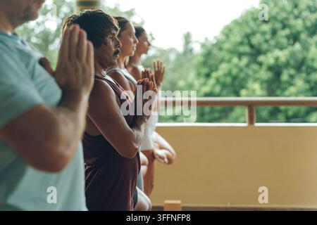 Persone in una classe di yoga in posizione di preghiera durante una sessione di consapevolezza all'aperto Foto Stock