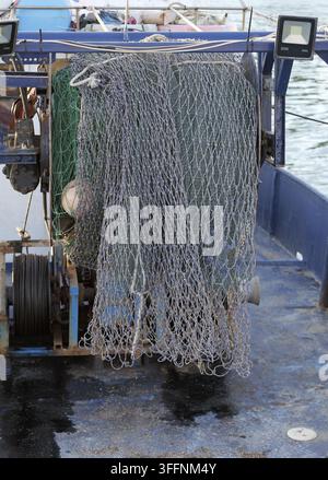 Rete da pesca appesa e in asciugatura sul ponte di una nave da pesca commerciale specializzata, con attrezzature industriali per un'industria marittima sostenibile Foto Stock