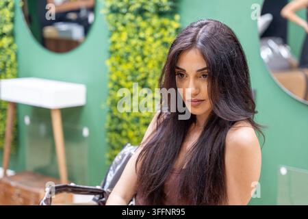 Donna con lunghi capelli scuri seduta in un ambiente moderno di salone di parrucchiere Foto Stock
