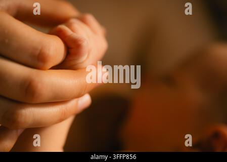 La piccola mano di un neonato che afferra il dito di un adulto, simboleggiando il legame prezioso, la cura genitoriale, l'affetto e la sensazione di sicurezza del sostegno familiare Foto Stock