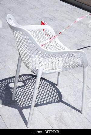 Sedia da esterno intrecciata bianca che proietta un'ombra suggestiva sulla terrazza illuminata dal sole Foto Stock