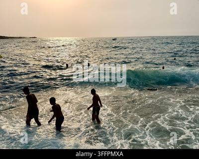 Persone che nuotano nel Mar Mediterraneo al tramonto a El Haouaria, sulla penisola di Cap Bon in Tunisia, una meta costiera popolare nel nord della Tunisia Foto Stock