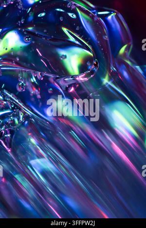 Vista macro astratta di vetro liquido iridescente con riflessi al neon luminosi, increspature traslucide, bolle e luci blu, verdi, rosa e viola Foto Stock