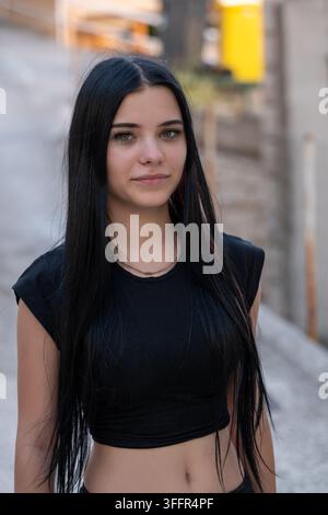 Una giovane donna con lunghi capelli neri si trova all'aperto in una luce naturale soffusa. Foto Stock