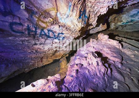 Formazioni rocciose ricoperte di graffiti illuminate da luce nera nella grotta di Cowboy Canyon Foto Stock