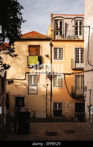 Facciate residenziali illuminate dal sole con balconi, finestre chiuse e biancheria su una strada acciottolata a Lisbona, Portogallo. Foto Stock