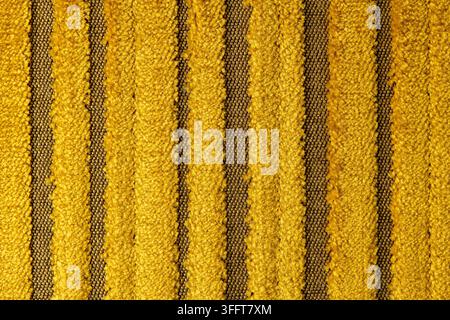 Una vista macro ravvicinata di una superficie in tessuto a strisce gialle e marroni che mostra dettagli di fili fini. Un'illuminazione morbida e uniforme evidenzia la consistenza opaca Foto Stock