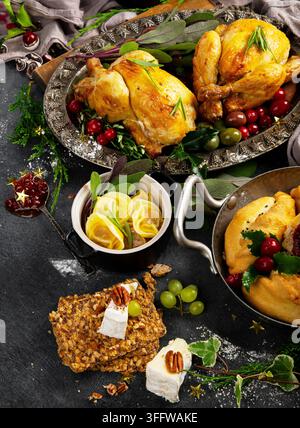 Impostazione della tavola per le festività natalizie con pollo arrosto, insalata, snack assortiti, olive e rami di pino su uno sfondo scuro. Vista dall'alto. Foto Stock