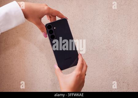 RIGA, LETTONIA. 25 agosto 2026. Persona che tiene il smartphone Samsung Galaxy S26 FE con entrambe le mani per presentare il design elegante del retro e la parte posteriore opaca Foto Stock