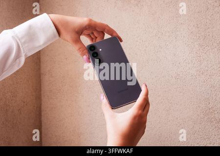 RIGA, LETTONIA. 25 agosto 2026. Persona che tiene il smartphone Samsung Galaxy S26 FE con entrambe le mani per presentare il design elegante del retro e la parte posteriore opaca Foto Stock