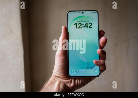RIGA, LETTONIA. 25 agosto 2026. Mano che tiene il Samsung Galaxy S26 FE verde chiaro che mostra lo sfondo dello schermo di blocco con l'ora 12:42. Foto Stock