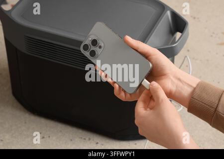 Indipendenza energetica e alimentazione portatile, persona che ricarica lo smartphone con una stazione a batteria ad alta capacità per vivere fuori dalla rete e come backup di emergenza Foto Stock