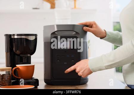 Indipendenza energetica e alimentazione di riserva, persona che utilizza una stazione di energia portatile per far funzionare gli elettrodomestici della cucina in un ambiente domestico Foto Stock