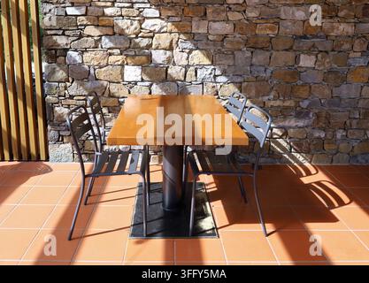 Tavolo di legno rustico con sedie in metallo nero. Muro in pietra sullo sfondo e pavimento piastrellato in terracotta. Foto Stock