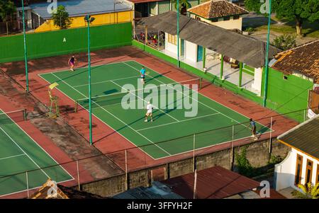 Vista aerea di persone che giocano a tennis su un campo verde circondato da edifici residenziali e mura a Kecamatan Prambanan, Jawa Tengah, Indonesia. Foto Stock