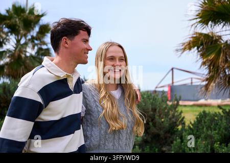 Giovane coppia sorridente che cammina insieme in una giornata soleggiata all'aperto. Foto Stock