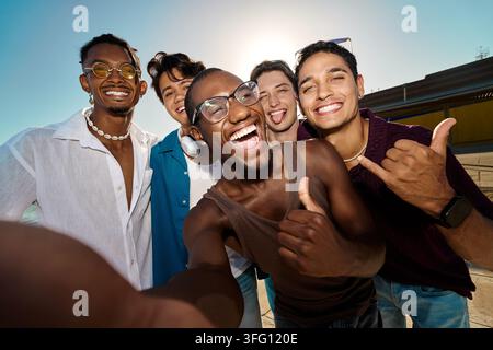 Gruppo vario di giovani uomini sorridenti che si scattano un selfie, esprimendo gioia e unità all'aperto in una giornata di sole Foto Stock