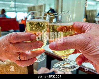 Prima vista ravvicinata di una coppia che brinda con bicchieri di champagne freddo in una lounge business class in aeroporto. Foto Stock