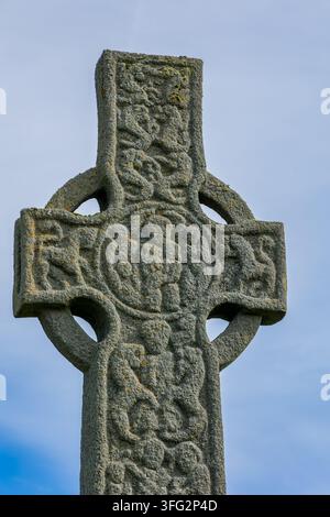 Testa e fusto di croce alta in pietra medievale con intricati motivi di nodi e intagli di figure bibliche, licheni che crescono sulla superficie di pietra erosa Foto Stock