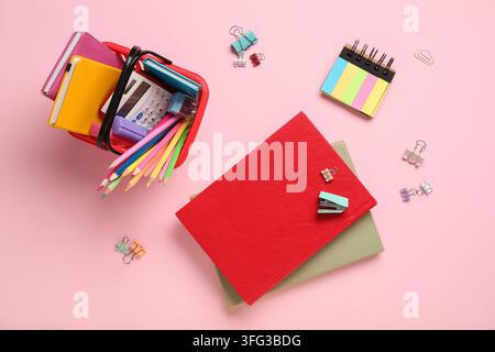 Acquisti per il ritorno a scuola e materiali didattici, cancelleria colorata in un piccolo cestino con quaderni su uno sfondo rosa per la pianificazione accademica Foto Stock