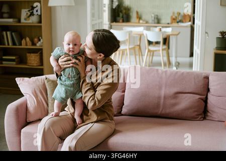 Madre felice che tiene un bambino seduta sul divano a casa Foto Stock