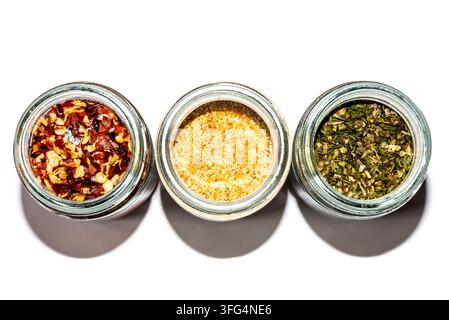 Composizione piatta concettuale. Tre barattoli di spezie contenenti peperoncino rosso, condimento giallo ed erbe verdi disposti per imitare un semaforo su uno sfondo bianco Foto Stock