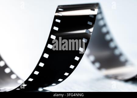 Primo piano minimalista di una striscia di pellicola fotografica 35mm arricciata sotto una luce intensa su uno sfondo pulito ad alto contrasto. Foto Stock