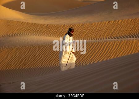 Ritratto di un uomo che ride con un foulard e una veste bianca in piedi su una cresta di duna di sabbia, governatorato di Dhofar, Rub al Khali, Oman Foto Stock