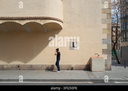 Uomo che cammina lungo un muro architettonico minimalista sotto il sole splendente Foto Stock