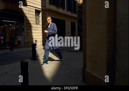 Uomo in giacca da lavoro blu che cammina su una strada cittadina soleggiata Foto Stock