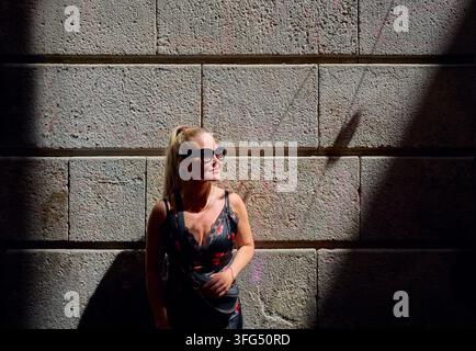 Donna elegante con occhiali da sole che godersi il sole davanti a un muro di pietra Foto Stock
