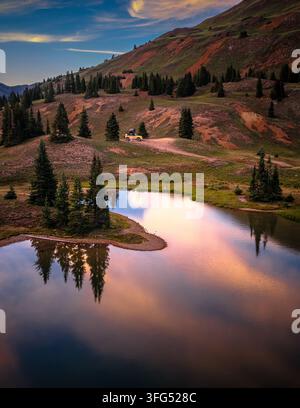 Camion off-road giallo parcheggiato vicino a un lago alpino al tramonto Foto Stock