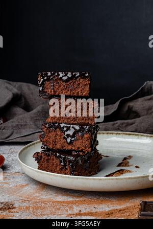 Pile di brownies al cioccolato fondente su un piatto di ceramica con basilico fresco Foto Stock