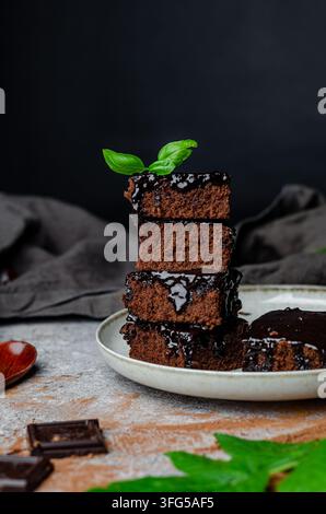 Pile di brownies al cioccolato fondente su un piatto di ceramica con basilico fresco Foto Stock