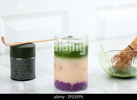 Ube Matcha Latte, bevanda vegetale superfood a strati alla moda con ghiaccio. Ube Halaya Matcha Latte colorato con ghiaccio, con bellissimi toni a strati o Foto Stock