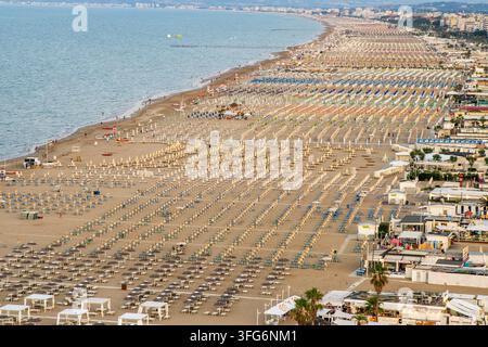 Italia, Rimini – 16 luglio 2025: Ampio resort balneare con spiaggia di sabbia fine, lettini e ombrelloni vista aerea sulla costa Foto Stock