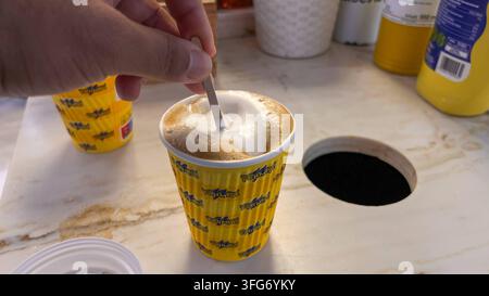 DATA DI REGISTRAZIONE NON INDICATA Braunschweig, Bassa Sassonia, Germania, Europa. Primo piano di una bevanda calda appena preparata in un bicchiere monouso. Una mano mescola il caffè con un bastoncino di legno, mentre la schiuma di latte copre la superficie. L'inquadratura mostra l'area del bancone di un bistrot o caffè della stazione con focus sulla bevanda e sul servizio da asporto. *** Braunschweig, Bassa Sassonia, Germania, Europa Primo piano di una bevanda calda appena preparata in un bicchiere monouso. Una mano mescola il caffè con un bastoncino di legno, mentre la schiuma di latte copre la superficie. La foto mostra l'area del bancone di un bistrot o caffè della stazione con focus sulla bevanda e sul servizio da asporto. Foto Stock