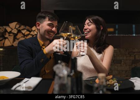 Una coppia felice celebra un'occasione speciale brindando con bicchieri di vino in un ristorante. Foto Stock