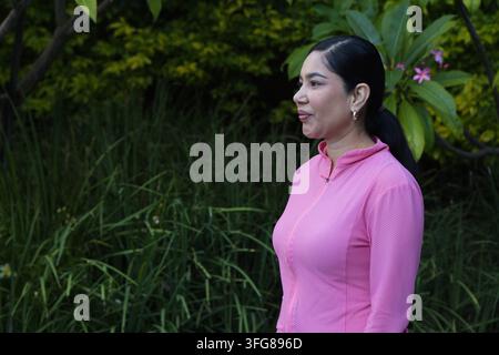 Donna adulta in piedi rivolta verso sinistra in giardino con giacca rosa brillante e fiore rosa, spazio per il testo Foto Stock