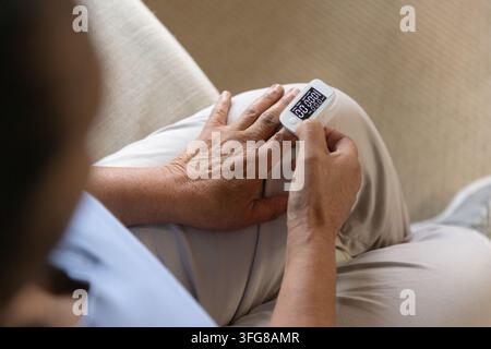 Ossimetro da dita bianco che misura la saturazione dell'ossigeno e la frequenza cardiaca sulle ginocchia, mani che regolano Foto Stock