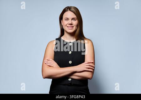 Donna d'affari sorridente in piedi con le braccia incrociate su uno sfondo azzurro Foto Stock