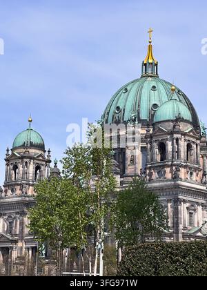 Vista ravvicinata del Duomo di Berlino con la sua grande cupola di rame verde, croce dorata e architettura storica ornata contro un cielo blu terso Foto Stock