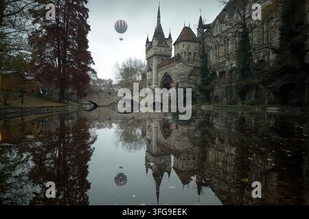 Mongolfiera che vola sopra il castello di Vajdahunyad con riflesso nell'acqua del lago nel parco cittadino di Budapest in autunno Foto Stock