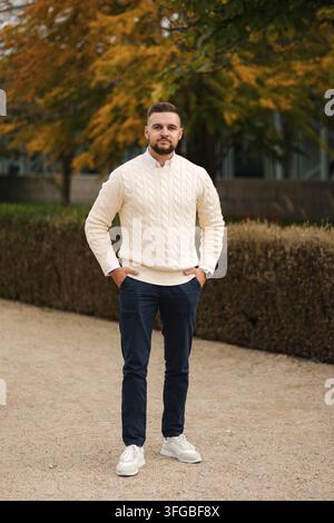 Prendersi un momento per rilassarsi all'aperto, un uomo vestito in modo casual si siede comodamente in un gilet elegante circondato dal fogliame autunnale. L'ambiente accogliente, naturale Foto Stock